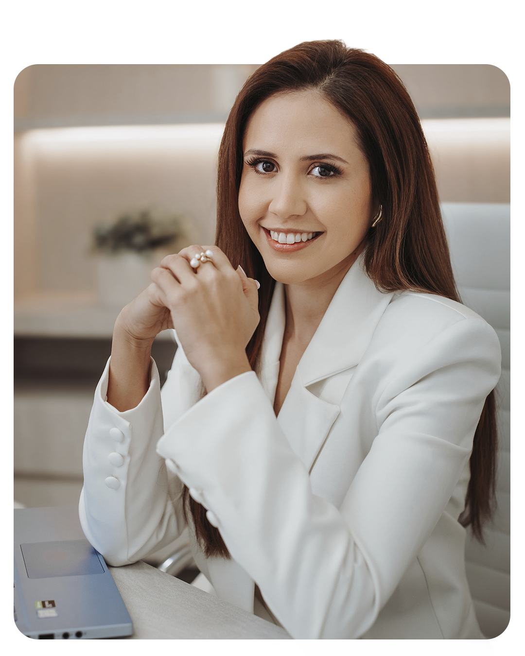 Dra. Daniella Andretta sorrindo, de blazer branco, em seu consultório